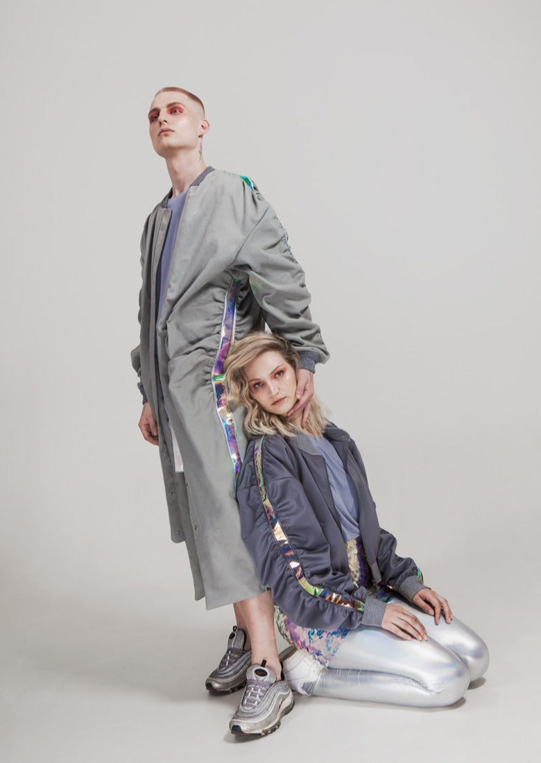 Front view of the MOON WALK coat from Cosmos Baby, featuring a long bomber-coat design in high-quality grey tech fabric with semi-transparent holographic PVC stripes on the sleeves and side seams